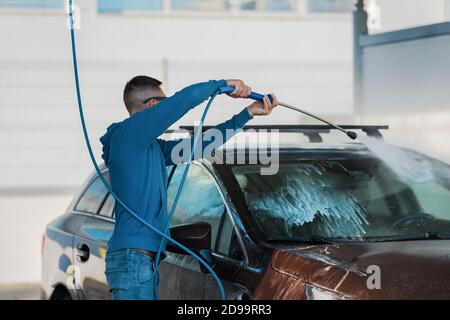 Homme lavant la voiture en libre-service. Nettoyage de la voiture à l'eau haute pression. Banque D'Images