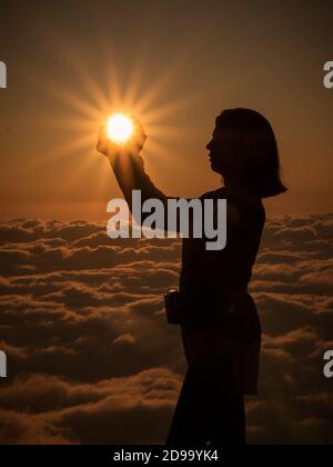 silhouette féminine au-dessus des nuages tenant le soleil avec des nuages Banque D'Images