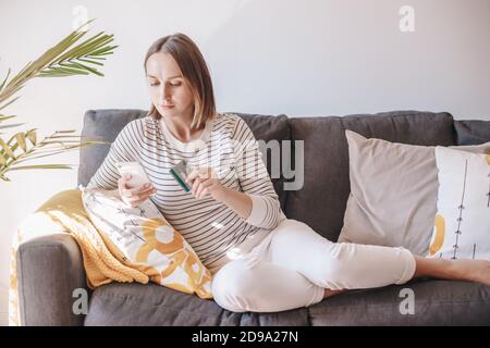 Moyenne âge Femme caucasienne shopping en ligne à partir de la maison. Jeune femme assise sur un canapé avec smartphone acheter des produits de la nourriture sur Internet et Banque D'Images