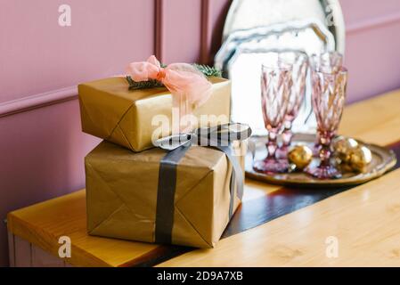 Boîtes-cadeaux avec rubans en papier artisanal sur l'arrière-plan de verres roses dans la salle à manger Banque D'Images