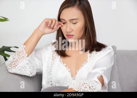 Les femmes asiatiques des vêtements de nuit en satin blanc grattent leurs paupières en raison de l'allergie dans une pièce. La femelle a un œil de démangeaison. Le concept de l'allergie Banque D'Images