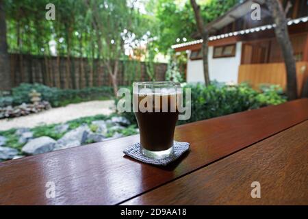 Verre de Hojicha glacé en gros plan, thé vert japonais rôti sur une table en bois avec vue sur le jardin de style zen Banque D'Images