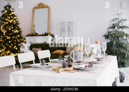 Belle table servie avec lanternes de sable décoration  LW AT  . Salle de séjour décorée de lumières et d'un arbre de Noël. Paramètre de vacances Banque D'Images