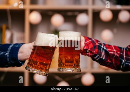 Deux tasses pleines de bière boivent dans les mains de deux mâles. Banque D'Images