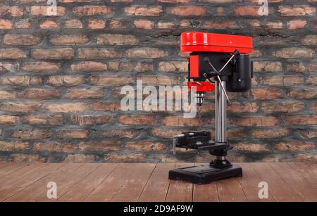 L'outil pour le travail des métaux - Nouvelle presse de forage rouge sur une table en bois et un fond de mur de brique. Banque D'Images