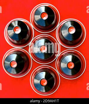 Vue aérienne des capsules noires et rouges disposées dans un motif floral symétrique, isolé sur un fond rouge. Banque D'Images
