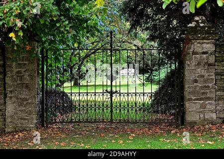 Entrée peu utilisée d'un grand jardin de campagne anglais, avec une clôture en fer forgé très ornée. Banque D'Images