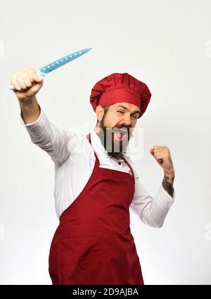 Cuisine et concept culinaire professionnel. Chef tient le couteau bleu vif vers le haut. Homme avec une barbe en uniforme de cuisinier isolé sur fond blanc. Cuisinez avec succès le visage dans un tablier bordeaux et un chapeau de chef. Banque D'Images
