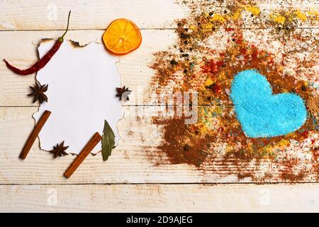 Concept de l'art alimentaire. Composition du condiment faisant la forme du coeur rempli de sel bleu. Morceau de papier avec bâtonnets de cannelle, étoiles anis et tranches d'orange sèches. Ensemble d'épices sur fond de bois beige. Banque D'Images