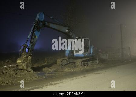 Excavatrice bleue travaillant la nuit dans la rue Banque D'Images