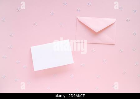 Carte de Noël vierge et enveloppe rose avec décorations de Noël sur une surface rose, vue du dessus. Maquette de l'espace de travail de l'hipster des fêtes, espace de copie. Banque D'Images