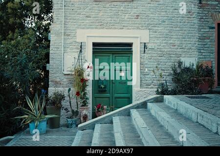 Une maison en brique avec une porte verte et des plantes derrière un escalier (Corinaldo, Marche, Italie) Banque D'Images