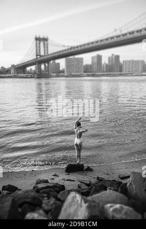 NEW YORK, États-Unis - 01 mai 2016 : image en noir et blanc d'une jeune femme en maillot de bain debout sur un rocher sur la rive de l'East River, sur le pont de Manhattan Banque D'Images