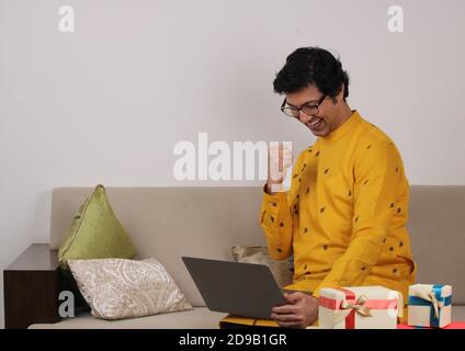 Jeune homme dans des lunettes et vêtements traditionnels assis à la maison à l'aide d'un ordinateur portable. Banque D'Images