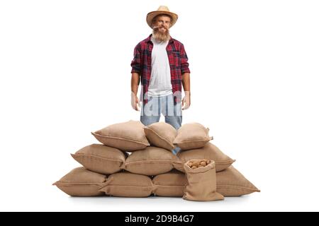 Joyeux fermier barbu debout derrière une pile de sacs de toile de jute avec pommes de terre isolées sur fond blanc Banque D'Images