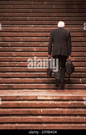 Homme âgé en tenue habillée grimpant les escaliers Banque D'Images