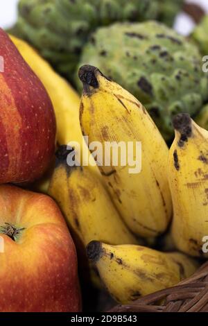 Pommes fraîches, bananes et pommes de crème anglaise gardées sur un panier en bois Banque D'Images