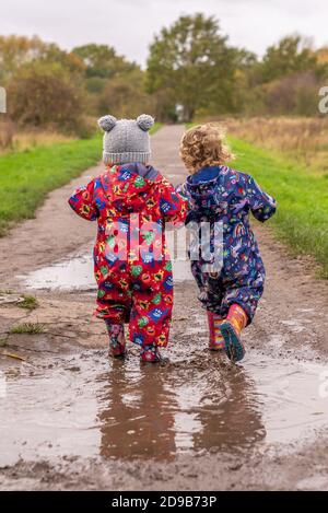 Deux petits enfants marchant dans une flaque de bottes wellington et tenues de protection Banque D'Images