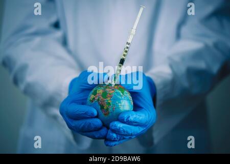 gros plan d'un médecin, portant un manteau blanc et des gants chirurgicaux bleus, vaccinant un globe terrestre Banque D'Images