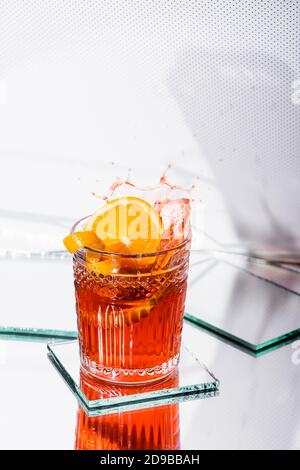zeste d'orange dans le verre avec cocktail d'alcool éclaboussé sur blanc Banque D'Images