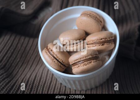 macarons dans un bol. macarons caramel sur un pull. photographie d'automne chaleureuse. photographie de nourriture dans des tons bruns. Banque D'Images