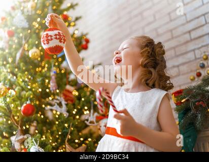 Joyeux Noël et joyeuses fêtes ! Mignon petite fille d'enfant est la décoration de l'arbre à l'intérieur. Le matin avant Noël. Banque D'Images