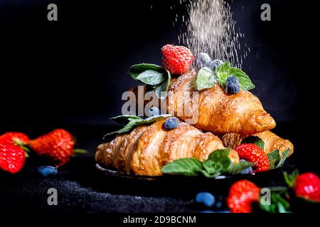 effet de déformation. Croissants sur fond sombre. Croissant avec baies. Petit-déjeuner français avec croissants. Croissants et baies saupoudrés de vache Banque D'Images