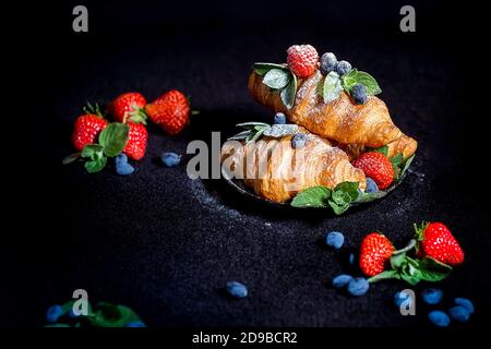 Croissants sur fond sombre. Croissant avec baies. Petit-déjeuner français avec croissants. Croissants et baies saupoudrés de sucre en poudre sur une d Banque D'Images