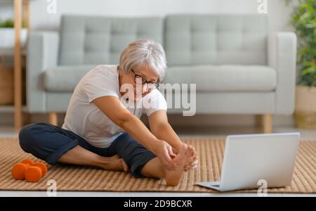 Femme senior en activité regardant des cours en ligne sur ordinateur portable tout en faisant de l'exercice à la maison. Banque D'Images