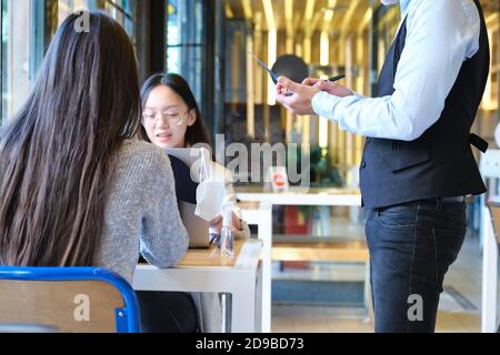 Serveur caucasien prenant la commande de clients dans un restaurant pendant l'épidémie de coronavirus. Nouvelle norme dans les restaurants. Pandémie de coronavirus. Banque D'Images