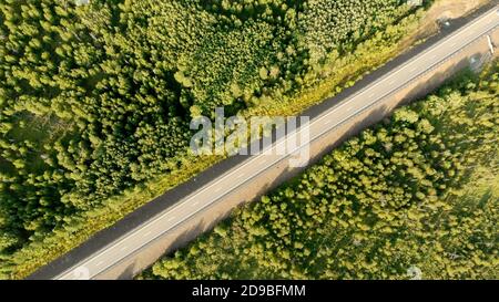 Vue aérienne des oiseaux sur une route de campagne vide entre la forêt verte par une journée ensoleillée. Vue panoramique depuis un drone sur un paysage naturel et une autoroute. Non t Banque D'Images