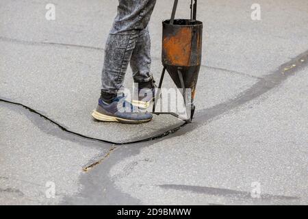 Travaux de restauration des ouvriers scellement des fissures application d'un produit d'étanchéité liquide sur l'asphalte une couche protectrice sur la route Banque D'Images