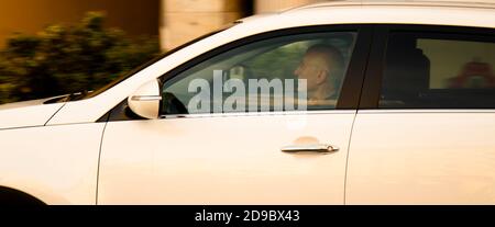 Belgrade, Serbie - 9 octobre 2020 : homme senior, conduisant une voiture blanche dans la rue de la ville, seule, à travers la fenêtre avec des reflets et des flous Banque D'Images