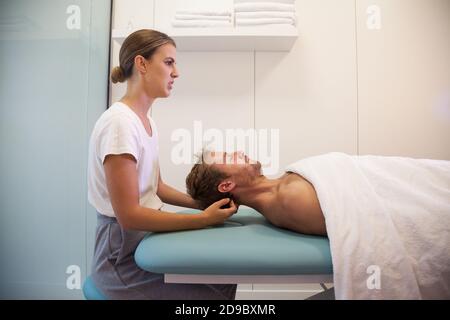 Kinésithérapeute féminin donnant un massage de la tête à un patient masculin Banque D'Images