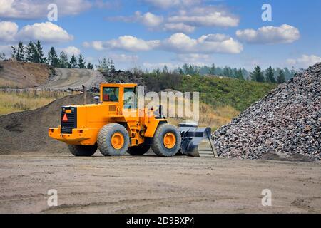 Chargeur de roue jaune en face de tas de rochers sur le chantier de construction sur une belle journée, espace de copie, pas de logos, pas de personnes. Banque D'Images