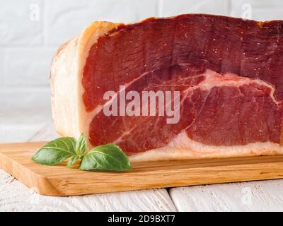 Grand morceau de jamon et feuille de basilic sur une planche à découper en bois. Jamon espagnol traditionnel Serrano. Délicieuse délicatesse de la viande. Gros plan. Vue avant. Banque D'Images