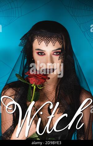 femme mal avec maquillage noir et voile foncé tenant rose près du lettrage de sorcière sur bleu Banque D'Images