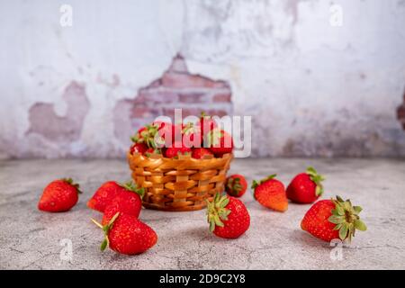 Fraises fraîches dans un petit panier sur fond de mur de briques. Banque D'Images