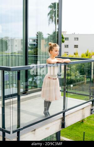 Jeune fille pensive rêvante portant une robe de danse. Enfant caucasien debout sur le balcon de la maison, regardant sur le côté réfléchi. Banque D'Images