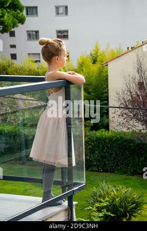 Jeune fille pensive rêvante portant une robe de danse. Enfant caucasien debout sur le balcon de la maison, regardant sur le côté réfléchi. Banque D'Images