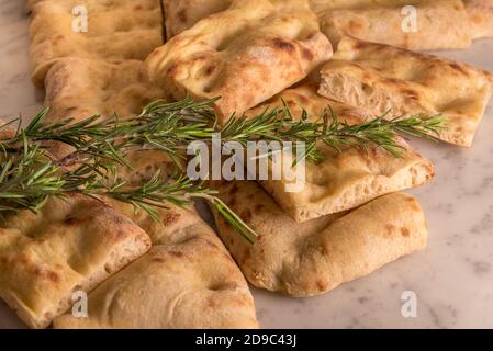 Pain italien de Focacia génoese tranché en morceaux carrés, pizza blanche et romarin frais sur une surface en marbre de Carrare Banque D'Images