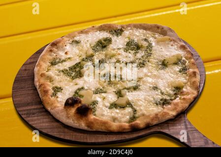 Pizza au pesto génois, pommes de terre et mozzarella sur planche à découper en bois sur fond jaune Banque D'Images