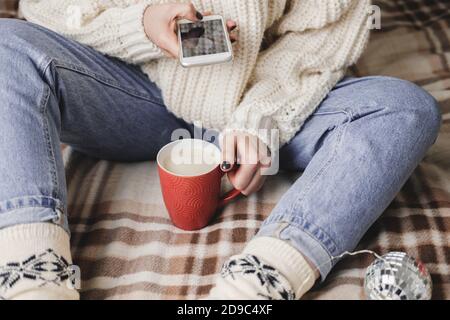 La main féminine avec smartphone prend des photos de la couverture du nouvel an ou de Noël pour les réseaux sociaux. Préparation des vacances, création de contenu. Tasse de cacao Banque D'Images