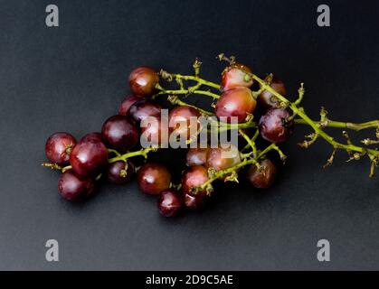 Raisins rouges pourris isolés sur fond de texture noire Banque D'Images