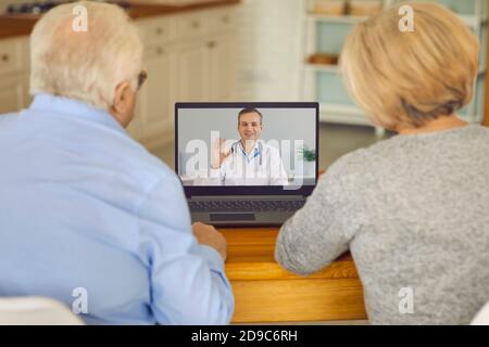 Vue arrière d'un couple senior assis devant un ordinateur portable et parlant à un médecin en ligne. Banque D'Images