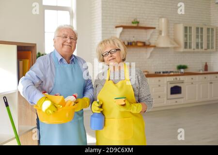 Couple de personnes âgées heureux en tabliers et gants debout et tenant équipement de nettoyage pour la maison Banque D'Images