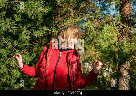 Belle femme dans une veste rouge dans un parc d'automne sur fond de pins Banque D'Images