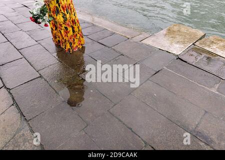 Dos d'une femme dans une robe jaune fleur marchant sous la pluie avec un bouquet de roses rouges dans les mains Banque D'Images