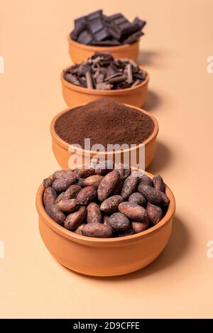 Fèves de cacao, poudre de cacao et chocolat dans des bols en céramique isolés sur fond beige. Concept des étapes de préparation du chocolat. Évolution du cacao. Banque D'Images