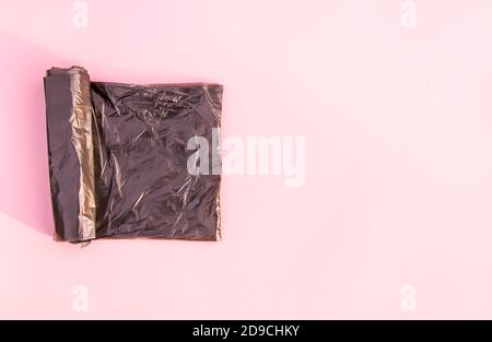 Le rouleau de sacs à ordures en plastique noir sur rose doux arrière-plan pastel Banque D'Images